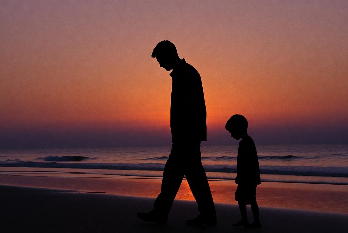 Father walks with son on beach with downcast expressions